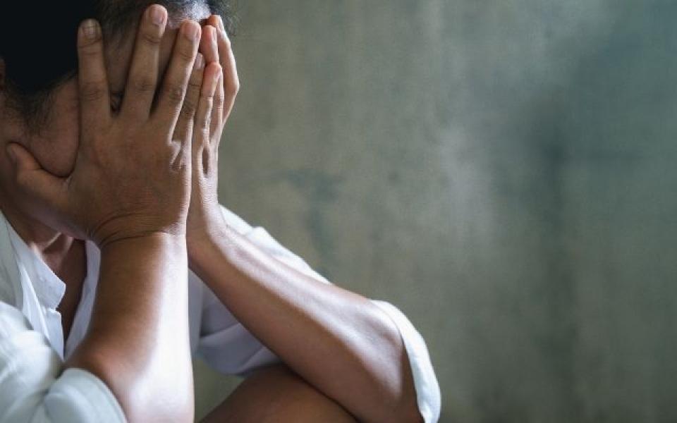 Woman sad, covering her face, on a grey background